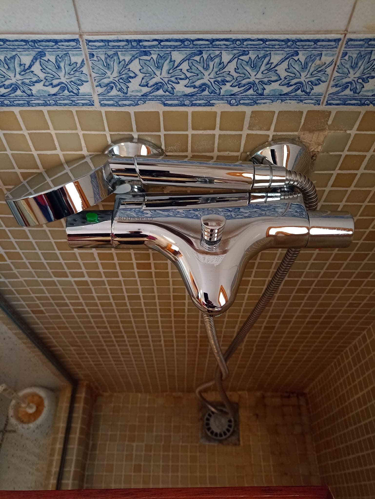 Grifo termostático cromado de una ducha, reluciente, sobre azulejos de gresite